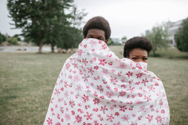 Funny dark skinned couple wrapped in sheet standing together outdoor in autumn park.  - Фото, изображение