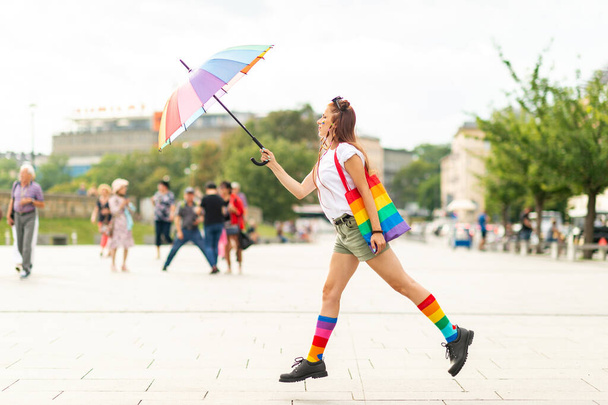 Lesbian in colorful lgbt socks and rainbow umbrella jumping at city square. - Photo, Image