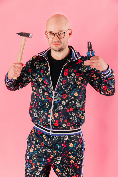Funny caucasian man with hammer and pliers in his hands posing on pink background - Zdjęcie, obraz
