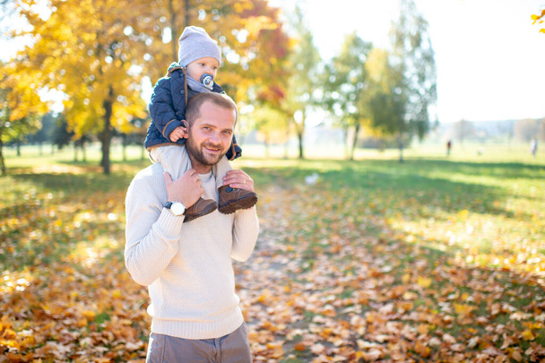 Happy father holding his beautiful child on his shoulders in autumn park. - Fotoğraf, Görsel