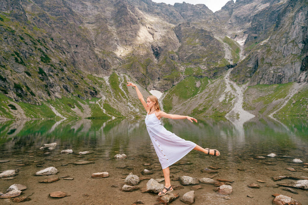 Portrait of blonde girl balancing at stone in lake among mountains. - Φωτογραφία, εικόνα