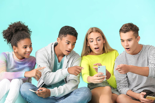Zaskakujące nastolatki z nowoczesnymi telefonami komórkowymi na kolorowym tle - Zdjęcie, obraz