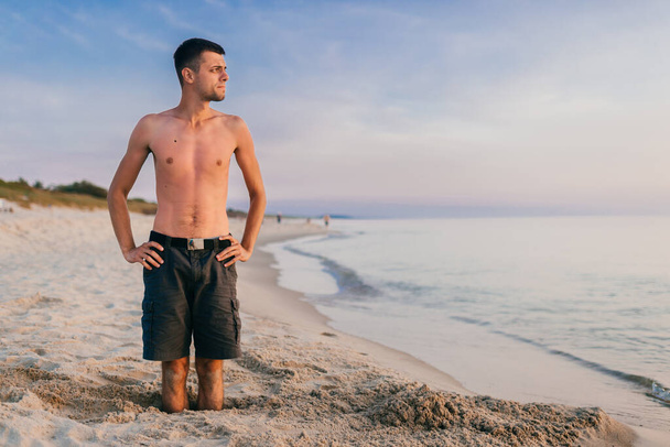 Young man standing in hole on the beach. - 写真・画像