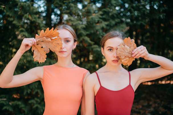 Two young girls standing outdoor with leaves in their hands covering their eyes. - Φωτογραφία, εικόνα