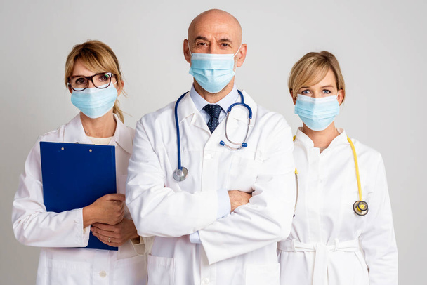 Shot of female and male doctors standing together at isolated background. Medical team. Doctors wearing face masks for prevention. - Foto, imagen