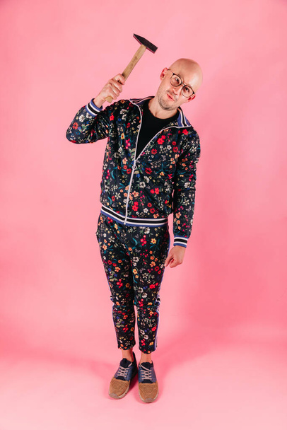 Funny fashionable man with hammer in his hand striking his head on pink background - 写真・画像