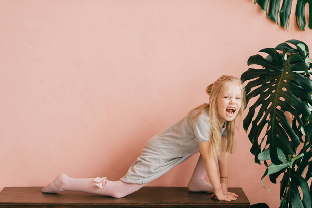 Beautiful little blonde long haired child girl in white tights posing for camera with excited funny face on pink wall background. Comical female child make faces and having fun in studio - Foto, Imagem