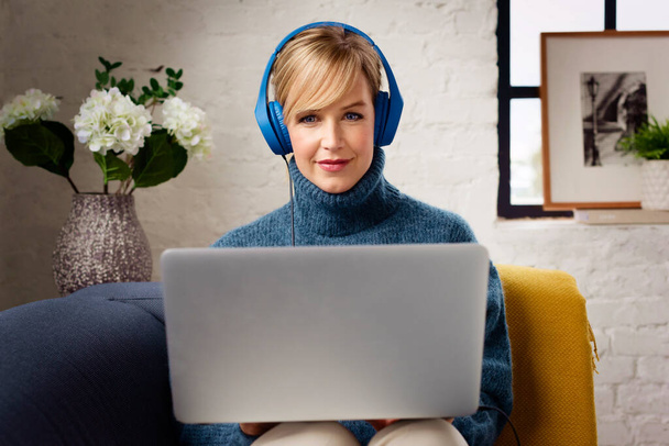 Portrait shot of beautiful smiling woman with headphone watching movie on laptop while sitting on the sofa at home. - Foto, Imagen