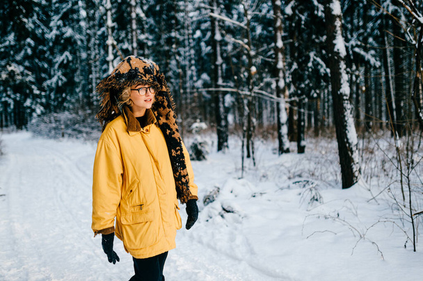 Funny strange young hipster girl with glasses and the scarf covering the head walking in the snow forest - Valokuva, kuva