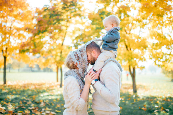 Family couple kissing outdoor with their baby sitting on fathers shoulders. - Foto, afbeelding