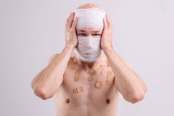 Injured man with many patches on his body and bandaged head isolated on white background - Zdjęcie, obraz