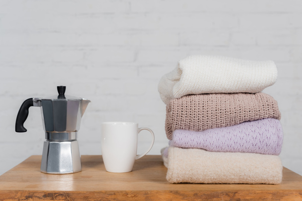 Coffee maker, cup and woolen sweaters on wooden table  - Photo, Image
