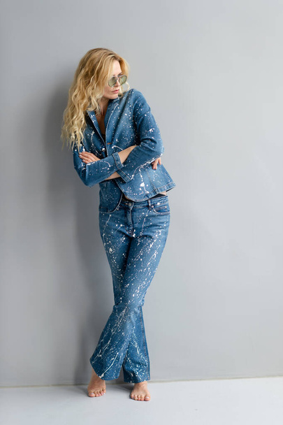 Beautiful stylish blonde model in jeans suit posing in studio - Foto, afbeelding