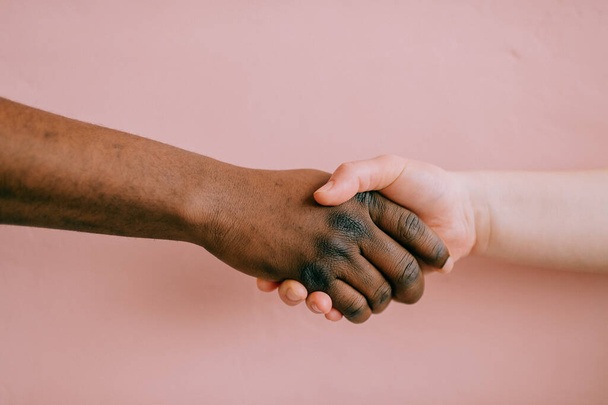 Handshake between african and caucasian male and female over pink background - Foto, Imagen