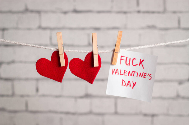 Valentine's day composition. Red hearts hanging on the clothespins. with a note "Fuck Valentine's day". Conceptual image for February 14th. Hate Valentine's  - Fotoğraf, Görsel