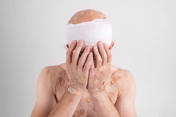 Injured man with many patches on his body and bandaged head isolated on white background - Fotó, kép