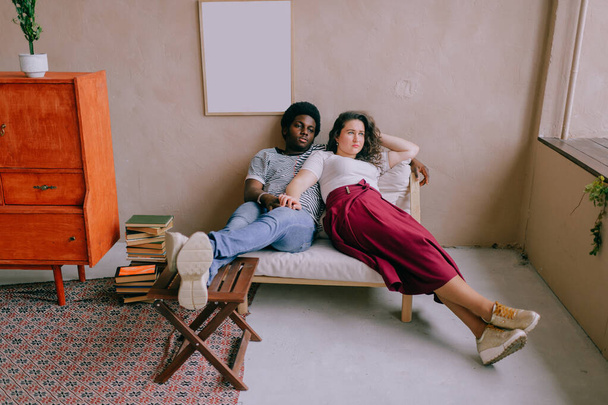 Loving interracial couple relaxing in chair in home interior. - Fotografie, Obrázek