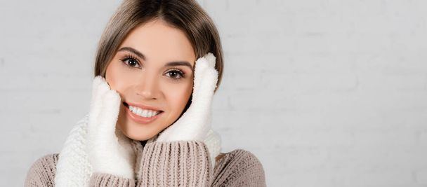 Mujer sonriente en suéter de punto y guantes suaves mirando a la cámara sobre fondo blanco, pancarta  - Foto, Imagen