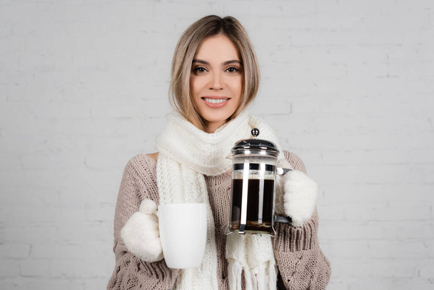 暖かいセーター、スカーフ、手袋の笑顔の女性は白い背景にカップとコーヒーポットを保持 - 写真・画像