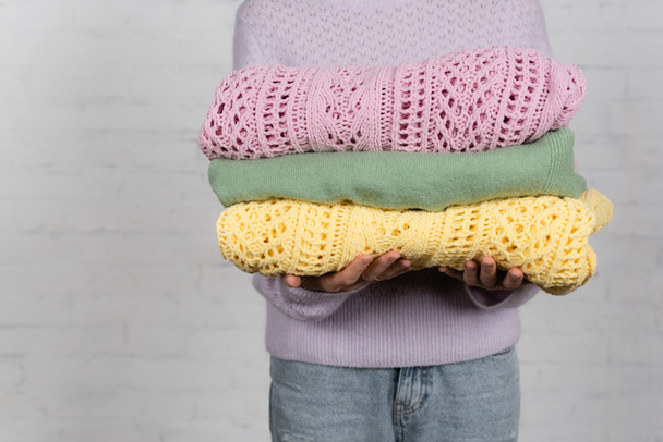 Cropped view of woman holding knitted sweaters on white background - Fotó, kép