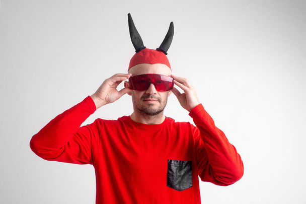 Strange devilish man in sunglasses and black red halloween costume posing over white background. - Foto, afbeelding