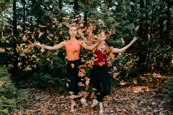 Portrait of two elegant ballerinas in black leggings pants, tutu and pointe shoes throwing up leaves and posing with happy smiling faces. - Foto, Bild