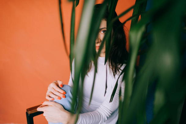 Imagem de uma mulher bonita com cabelo preto em uma jaqueta branca e comprimentos senta-se em uma cadeira e olha para a planta - Foto, Imagem