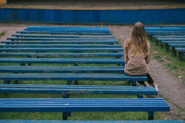Back portrait of lonely girl sitting on bench with rows of desolate benches on background. - Foto, immagini