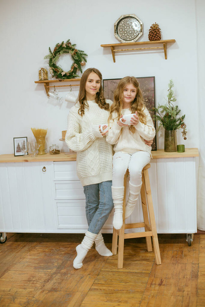 girls in warm light knitted sweaters in the kitchen with cups of warm cocoa - Foto, Bild