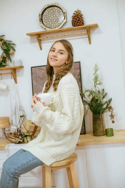 girl in warm light knitted sweaters in the kitchen with cups of warm cocoa - Valokuva, kuva