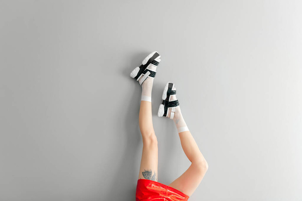 Beautiful female legs in white mesh trendy socks wearing fashionable black white high wedge leather sandals. Womens modern fashion footwear. Rebel girl in red leather skirt on gray background - 写真・画像