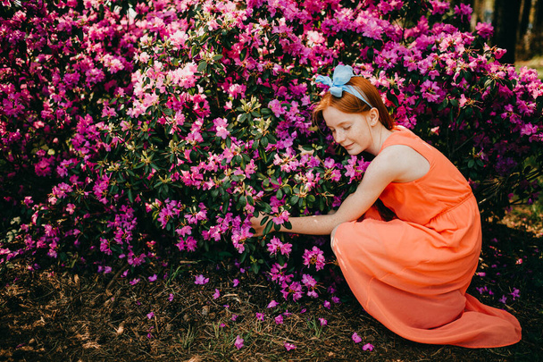 Picture of an amazing red-haired baby girl in an orange dress enjoying a pastime in the big spring garden. - Fotoğraf, Görsel