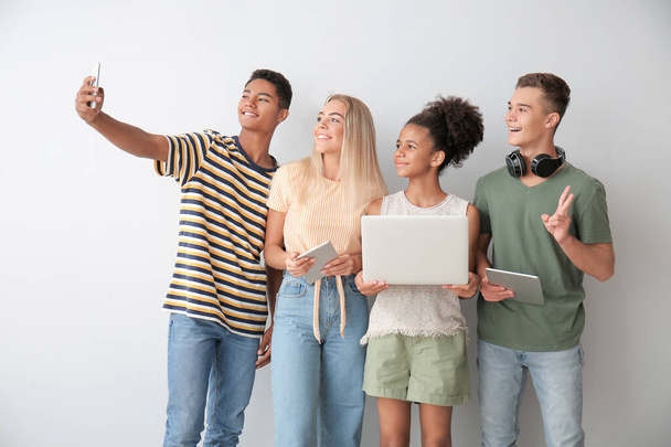 Teenagers with different devices taking selfie on light background - Foto, Imagem