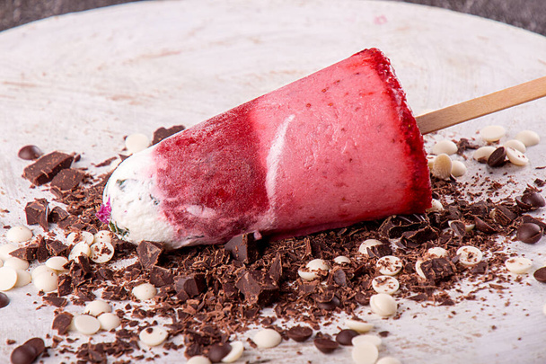 Crème glacée aux fraises popsicle sucettes avec crème fouettée chocolat décoré sur fond blanc en bois.  - Photo, image
