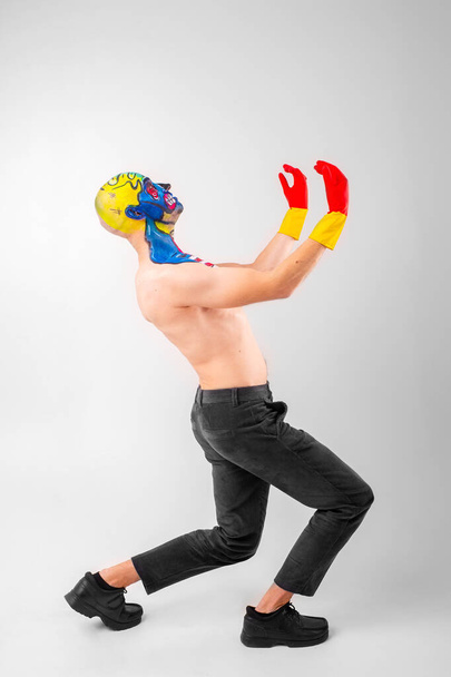 Strange man with makeup on his head and shoulder in white t-shirt, red and yellow gloves, red gesticulates - Фото, изображение