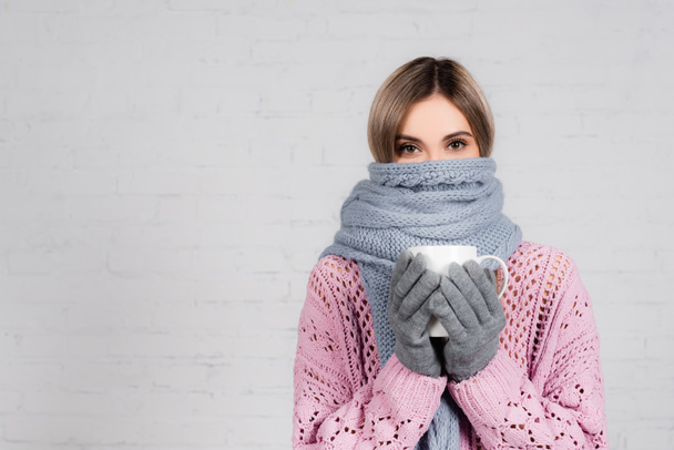 Woman in warm sweater, scarf and gloves holding cup on white background - 写真・画像