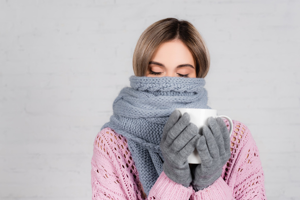 Young woman wrapped in warm scarf holding cup on white background - Фото, зображення