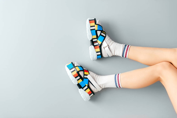 Beautiful female legs in white trendy socks posing in colorful fashionable high wedge leather sandals on gray background. Asian anime style concept. Womens legs wearing high sole summer stylish shoes - Photo, Image