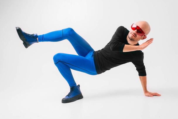 Fashion portrait of stylish man in blue tights and indigo boots stretching and exercising over white studio background. - Φωτογραφία, εικόνα