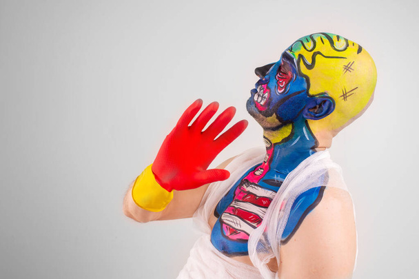 Strange man with makeup on his head and shoulder in white t-shirt, red and yellow gloves, red gesticulates - Foto, Imagem