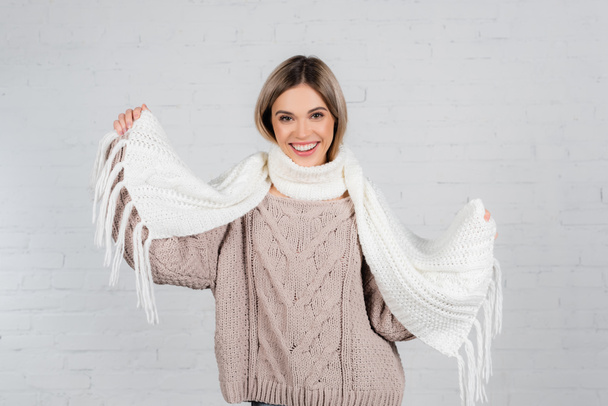 Усміхнена жінка в в'язаному светрі тримає шарф на білому тлі
 - Фото, зображення