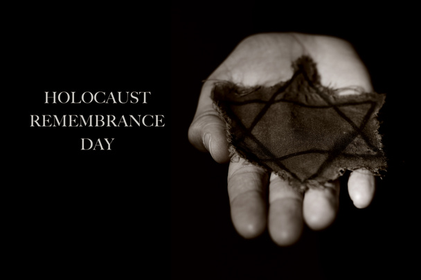 Nahaufnahme des Davidsterns in einem alten, zerlumpten Abzeichen an der Hand eines Mannes, und der Text Holocaust-Gedenktag auf schwarzem Hintergrund - Foto, Bild