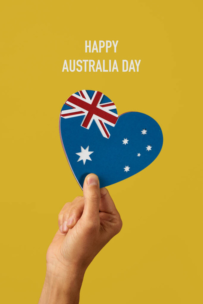 lähikuva miehen kädestä, jolla on Australian lipun muotoinen sydän, joka on valmistettu erivärisistä paperinpaloista, ja teksti onnellinen australialainen päivä keltaisella pohjalla - Valokuva, kuva