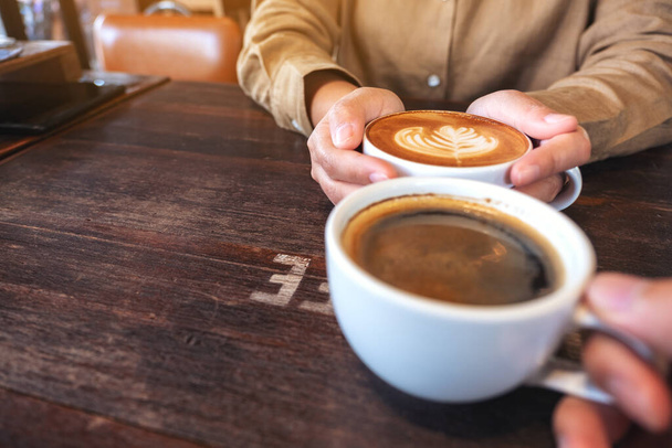 Immagine in primo piano di due persone che tengono tazze bianche di caffè caldo su tavolo di legno in caffè - Foto, immagini