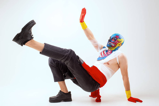 Strange man with makeup on his head and shoulder in white t-shirt, red and yellow gloves, red dances - Фото, изображение