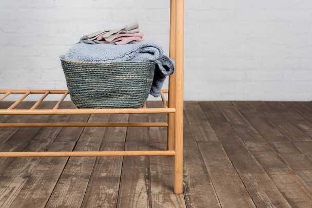 Basket with knitted sweater and gloves on hanger rack  - Φωτογραφία, εικόνα