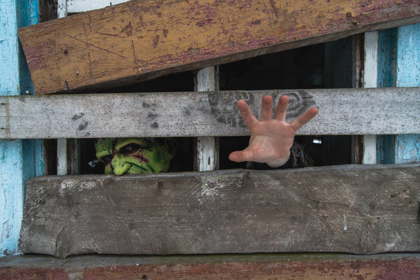 Egy szörnymaszkos emberről készült kép kinyújtja a kezét, még ha egy öreg, koszos, bedeszkázott ablak is van a faluban. - Fotó, kép