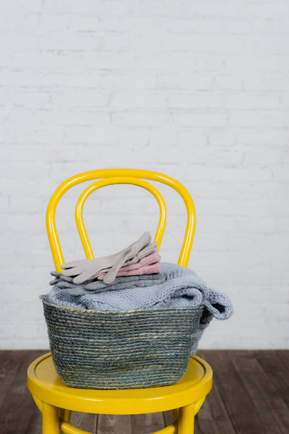 Korb mit Handschuhen und Pullover auf Stuhl zu Hause  - Foto, Bild