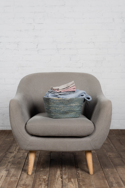 Basket with warm sweater and soft gloves on armchair  - Valokuva, kuva