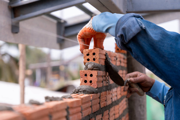 Trabajador albañil instalando mampostería de ladrillo pared exterior con paleta cuchillo masilla en el sitio de construcción - Foto, imagen